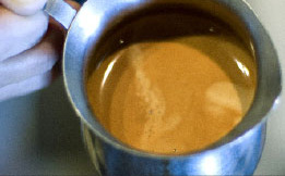 A fresh shot of espresso with golden crema in a metal pitcher