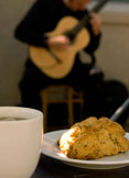 A scone and a cup of coffee on a table, with a guitarist playing in the background