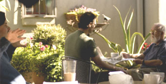 Friends in conversation around a patio table surrounded by greenery