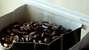 Glossy dark-roasted beans filling a kraft paper bag