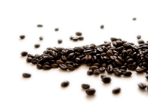 A scattering of dark-roasted coffee beans on a white surface